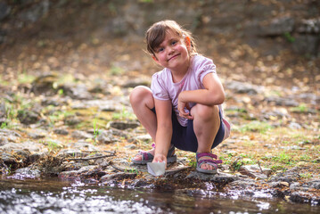 Young girl launching paper boat into creek in forest