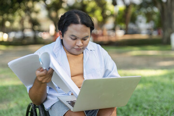 Obraz premium Young Disabled Businessman in Wheelchair Reviewing Outdoor Work on Laptop in a Park Setting