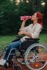 Woman in wheelchair drinking water in a park