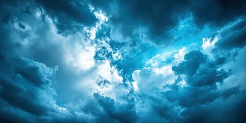 Obraz premium Dramatic sky with deep blue tones and varying gray clouds creating an atmospheric backdrop, with bright highlights peeking through.