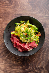 A close-up of a delicious salad featuring fresh greens and tender slices of roast beef in a dark bowl, set against a wooden background. Perfect for food-related content.