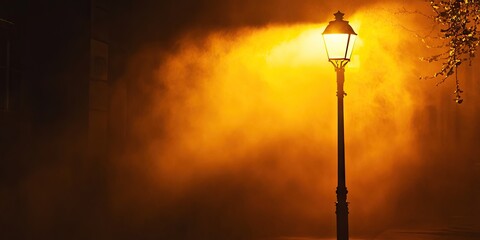 Street lamp illuminated by amber light in dense fog creating a mystical atmosphere with warm yellow tones dominating the scene.