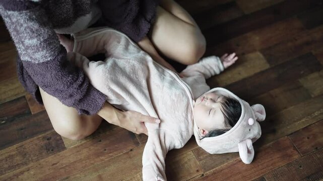 In a warm winter Japanese apartment room, a 6-month-old Japanese girl wearing fluffy clothes and her mother are sitting on the floor, holding the sleeping baby and trying to place it on the floor.