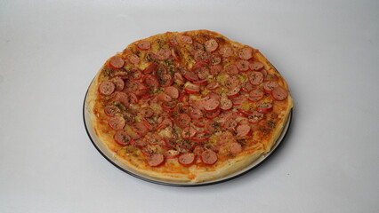 One pan pizza topped with beef sausage served on a white round plate and placed on a white table and background.