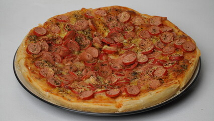 One pan pizza topped with beef sausage served on a white round plate and placed on a white table and background.