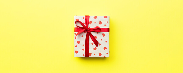 Gift box with red ribbon and heart on yellow background, top view with copy space for text