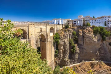 Wall murals The Puente Nuevo bridge in El Tajo gorge in Ronda town in Spain. Ancient stone bridge spanning a deep gorge, with a white village perched on the cliffside. Sunny day, scenic view.