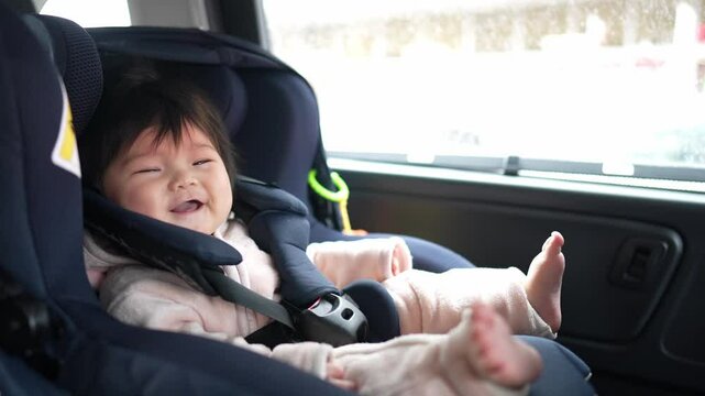 A 6-month-old Japanese baby girl is sitting in a baby seat in the back seat of a car. Slow motion video.