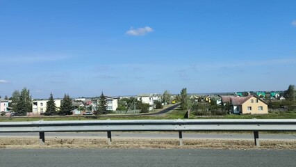 the car is in motion, the view from the window. Autumn landscape, road, residential buildings in rural areas, view from the car window