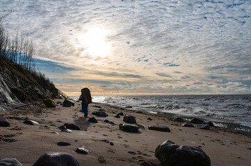 Take A Hike Day. WORLD TOURISM DAY. Man with Backpack hiking in beautiful windy coastal dune marram grass towards beach of Baltic Sea in soft evening sunset sunlight.