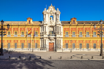 Obraz premium The Palace of San Telmo in Seville town, capital of Andalusia in Spain. Grand palace facade with ornate details, under a bright blue sky. Flags fly proudly.
