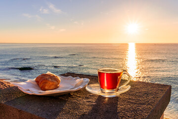 concept of street outdoor breakfast with a cup of tea or coffee on a morning coast during sunrise. landscape of city embarkment with sea water and cloudy sky on background