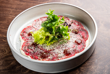 A beautifully plated carpaccio featuring thin slices of beef, topped with fresh greens and a sprinkle of cheese. A gourmet dish perfect for fine dining or culinary presentations.