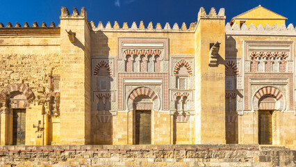 The Mosque–Cathedral of Cordoba, Cathedral of Our Lady of the Assumption in Cordoba town in Spain. Ancient architecture with intricate stonework and arched doorways bathed in sunlight.