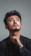 Fototapeta premium Pensive Asian man gazes up with thoughtful expression, contemplative moment Generated AI