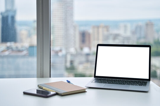 Open laptop mock up screen on work table, modern computer technology device in skyscraper luxury executive office with desk, chair and big window city view, workspace background.