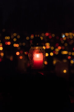 A Grave Candle Glowing On The Top Of A Gravestone With Red Light On All Saints' Day Night. A Bunch Of Blurry Grave Candles In The Background