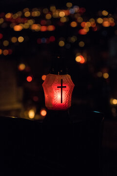A Grave Candle With A Cross On It Glowing On The Top Of A Gravestone With Red Light On All Saints' Day Night. A Bunch Of Blurry Grave Candles In The Background