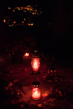 A Bunch Of Grave Candles Glowing With A Red Light On A Gravestone On All Saints' Day In The Night, Blurry Grave Candles Glowing In The Background