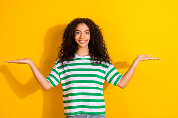 Portrait of pretty young girl hold empty space vs wear striped t-shirt isolated on yellow color...