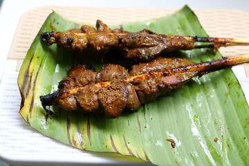 Close up two bamboo stick clamp chicken's livers grilled on banana leaf on table.