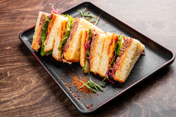 A delicious sandwich stacked with layers of fresh vegetables and savory fillings, served on a black plate. Perfect for appetizing food photography and culinary presentations.