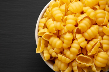 Homemade Dry Raw Gnocchi Pasta in a Bowl on a black background, top view. Flat lay, overhead, from above. Copy space.