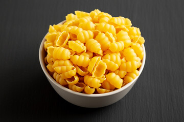 Homemade Dry Raw Gnocchi Pasta in a Bowl on a black background, side view.