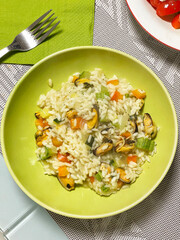 Risotto with vegetables and mussels on green plate at home. Vegetables and seafood. National cuisine of Europe. 