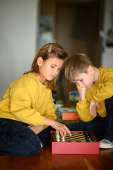 Naklejka premium A boy and a girl play chess together, focused and engaged in the game. The scene reflects concentration and friendly competition, showcasing the fun of strategic thinking and mental challenge.