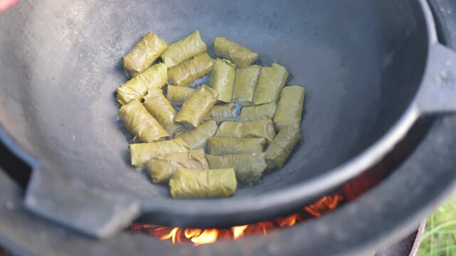 Vegetables, grape leaves stuffed with minced meat, are boiled and stewed in a cauldron and steam goes over them