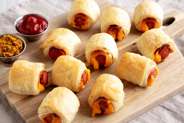 Homemade Pigs in a Blanket with Ketchup and Mustard on a Wooden Board, side view.