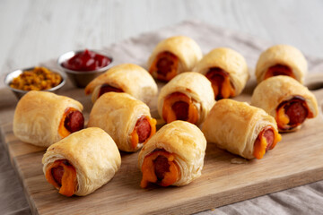Homemade Pigs in a Blanket with Ketchup and Mustard on a Wooden Board, side view. Close-up.
