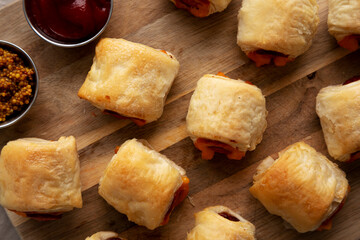 Homemade Pigs in a Blanket with Ketchup and Mustard on a Wooden Board, top view. Flat lay, overhead, from above.