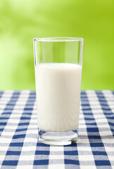 Glass of milk on checkered table cloth, green background