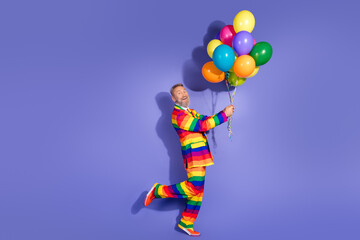 Joyful elderly man in vibrant rainbow suit holding colorful balloons against a purple background, embodying freedom and diversity