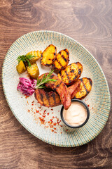 A vibrant plate featuring grilled tongue and potatoes, accompanied by pickles, red onions, and a dipping sauce. Perfect for food-related projects showcasing delicious meals.