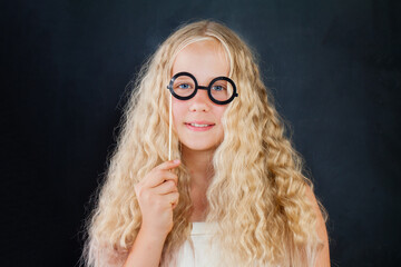 Attractive young girl posing with photo booth props glasses on black background