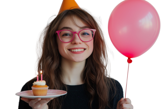 Portrait of a smiling young woman wearing pink glasses and a party hat, holding a balloon. She is also holding a plate with a cupcake and a candle on a transparent background