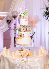 Wedding cake with the letters love on top. Beautiful wedding cake with white cream decorated with flowers and sugar butterflies. Elegant three-tiered wedding cake with candles around it at the banquet