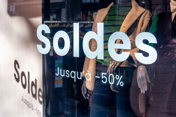 Gros plan d'un marquage "Soldes jusqu'à -50%" écrit en français sur la vitrine d'un magasin de vêtements situé en France, pendant la période des soldes