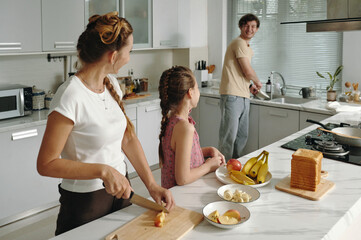 Happy family cooking breakfast together in the kitchen with little girl helping her parents