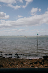 A sailboat is sailing in the ocean near a green buoy. The sky is cloudy, but the water is calm