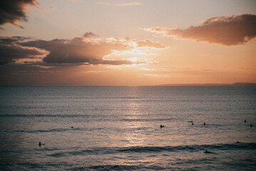 Obraz premium The sky is a beautiful orange color as the sun sets over the ocean. The water is calm and the surfers are enjoying the sunset