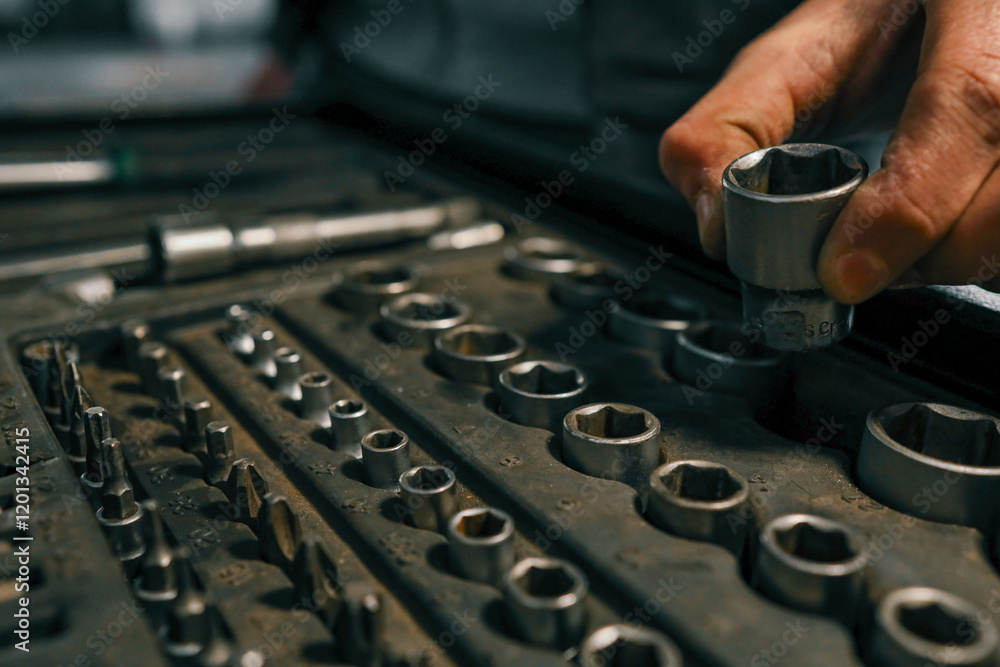 Poster hand selecting a metal socket wrench piece from an organized tool tray in a workshop setting, symbol