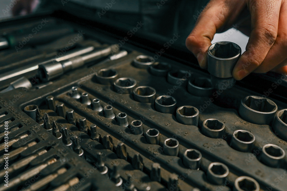 Poster hand selecting a metal socket wrench piece from an organized tool tray in a workshop setting, symbol
