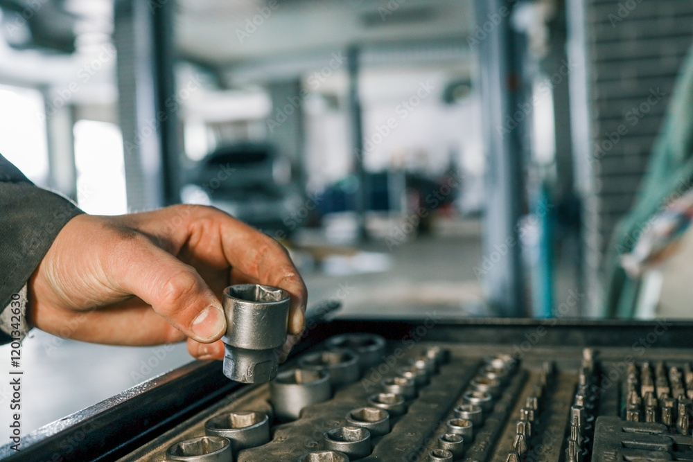 Poster hand selecting a metal socket wrench piece from an organized tool tray in a workshop setting, symbol