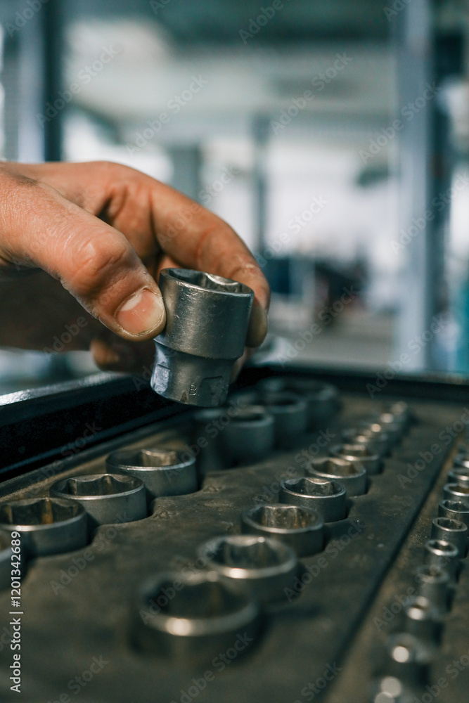 Poster hand selecting a metal socket wrench piece from an organized tool tray in a workshop setting, symbol