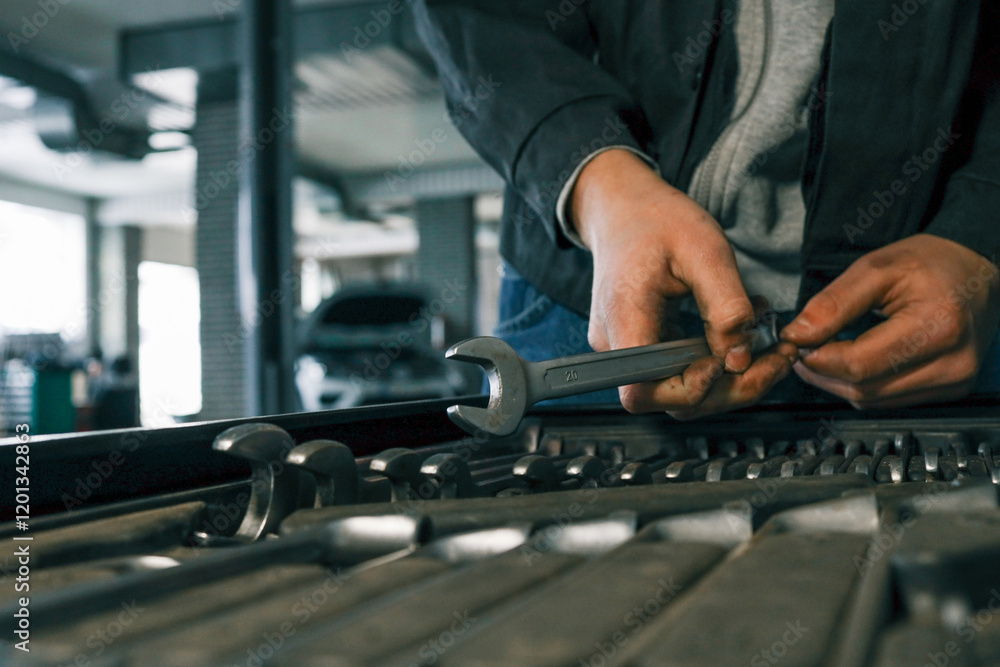 Poster mechanic selecting a wrench from a tool tray in a garage, preparing for vehicle maintenance or repai