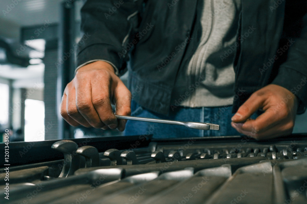 Poster mechanic selecting a wrench from a tool tray in a garage, preparing for vehicle maintenance or repai